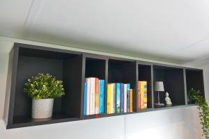 a black book shelf with books and a potted plant at Tinyhouse Seeträumchen direkt am See mit Terrasse für 4 in Bodenwöhr