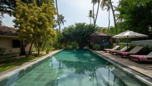 a swimming pool with chairs and an umbrella next to a house at Coconut Grove - 4 Bed Pool Villa with Cook in Ahangama