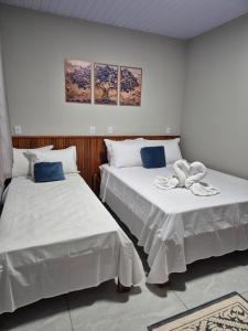 two beds in a room with white sheets and blue pillows at Pousada Paraiso valle verde in Estivado