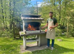 a man in an apron standing next to a grill at LE GRIZZLY Chalet en bois avec SPA Jacuzzi in La Bresse