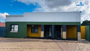 a green and yellow building on a brick street at Village Boiketlo in Bloemfontein