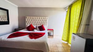 a bedroom with a bed with red pillows and yellow curtains at Village Boiketlo in Bloemfontein