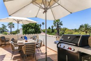 a patio with a table and an umbrella and a grill at Casa Juniper in Praia do Carvoeiro