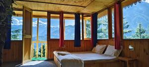 a bed in a room with windows and mountains at Jibhi Pine Nature Tree house in Jibhi