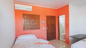 a bedroom with orange walls and a bed and a bathroom at Suite em Guriri Norte com Piscina e Conforto in São Mateus
