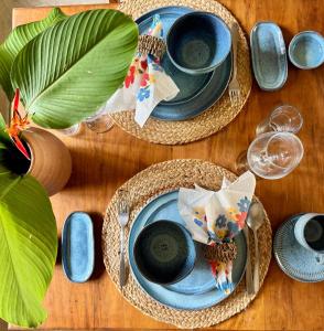 a table with two blue plates and glasses and plants at Casa Preguiça Corumbau in Corumbau