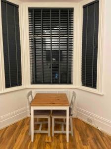 a table and two chairs in a room with two windows at Self Contained Studio Flat Acton Central West London in London