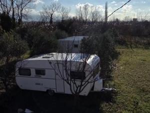 a white trailer parked in a field next to a bush at Unique night in a cozy caravan in Lezhë