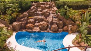 a man in a swimming pool with a rock waterfall at Hotel Sanctuarium Adults Only in Fortuna