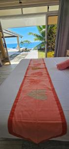 a bed with a red and white comforter on a beach at Raiatea Sunrise villa in Taputapuapea
