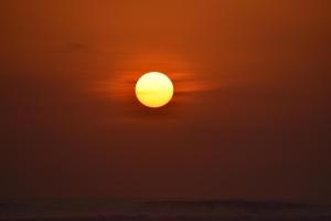 an orange sun in a cloudy sky over the ocean at La Posada - Hostel in Santa Teresa Beach