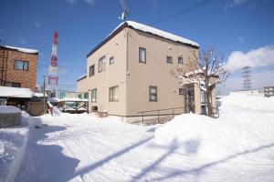a building with snow on the ground in front of it at Guest House Nishimiyanosawa in Teine