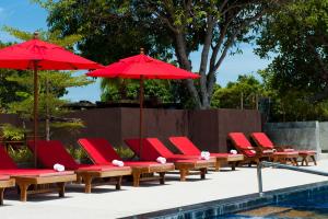 una fila di sedie a sdraio rosse e ombrelloni accanto alla piscina di Sea Garden Resort Haad Chao Phao a Haad Chao Phao