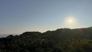a sun setting over a hill with trees and the ocean at Soiree in Zipolite