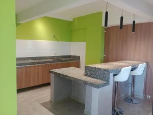 a kitchen with green walls and a counter and stools at Apartamento Studio in Barbacena