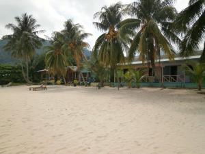 a building on the beach with palm trees in front at Rainbow Tioman Cottage in Kampong Juara
