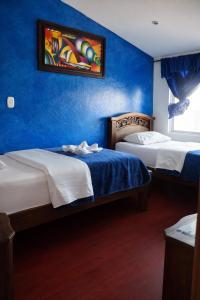 two beds in a room with a blue wall at Hotel Restaurante El Madroño Chia in Chía