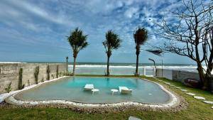 a swimming pool with two white chairs and the ocean at Beach Villas Phan Thiêt in Bình Sum