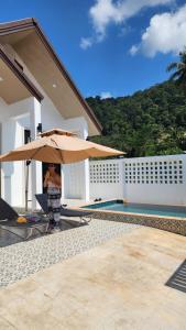 a woman standing under an umbrella next to a pool at Pana Villa Koh Lanta in Ban Ai Dao