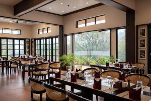 a restaurant with tables and chairs and large windows at Nirjhara Coorg in Somvārpet