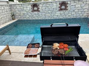 a grill with meat and vegetables next to a swimming pool at Detached house with pool in Alaçatı in Çeşme