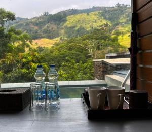 three glass bottles and cups on a table with a view at Romance Valley Haputale in Haputale