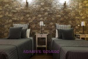 a bedroom with two beds and a stone wall at Apartamentos Adarve Toledo in Toledo