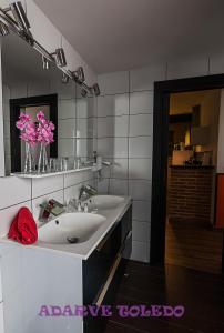a bathroom with two sinks and a mirror and pink flowers at Apartamentos Adarve Toledo in Toledo