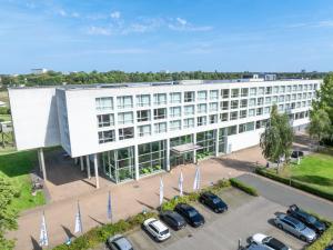 a large white building with cars parked in a parking lot at ATLANTIC Hotel Galopprennbahn in Bremen