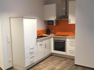 a kitchen with white cabinets and an orange wall at Boardinghaus Götterhimmel in Obernburg am Main