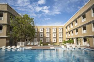 a swimming pool in front of a building with white chairs at Taj Lalit Bagh, Udaipur in Udaipur