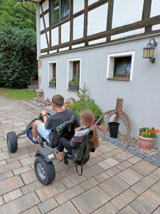 two children riding on a toy car outside a house at Ferienwohnung Hegemühle in Geithain +8 photos