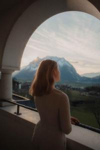 a woman looking out of a window at a mountain at IMLAUER Hotel Schloss Pichlarn in Aigen im Ennstal