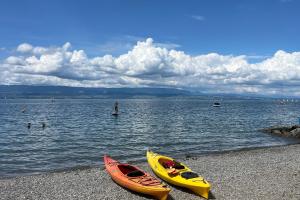 two kayaks on a beach with people in the water at Camping le Relais du Léman in Messery