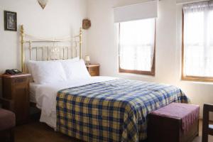 a bedroom with a bed with a plaid blanket and two windows at Hagiati Guesthouse - Edessa Cozy Mountain Retreat in Edessa