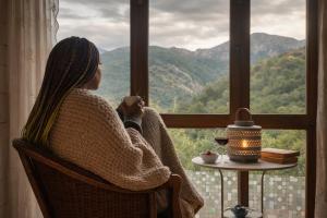a woman sitting in a chair holding a cup looking out a window at Carbayu Senda del Oso in Proaza