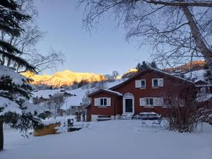 a red house in the snow with mountains in the background at Chalet Chic mit Hot Pot in Wildhaus