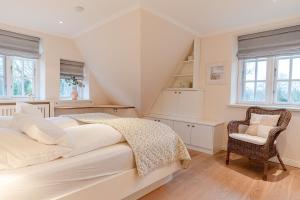 a white bedroom with a bed and a chair at Friesenliebe in Borgsum