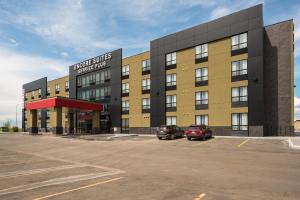 un grand bâtiment avec des voitures garées dans un parking dans l'établissement Encore Suites by Service Plus Inns, à Grande Prairie