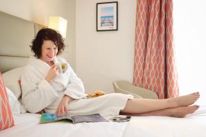a woman sitting on a bed drinking a cup of coffee at Hotel Nice Riviera in Nice