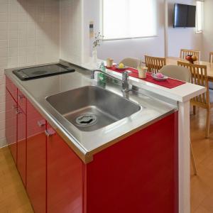 a kitchen with a stainless steel sink and red cabinets at Grand Reve KODEKI Near Nagoya Dome in Yadachō