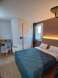 a bedroom with a large bed with a blue blanket at Premiere Classe Dunkerque Est Armbouts Cappel in Armbouts-Cappel