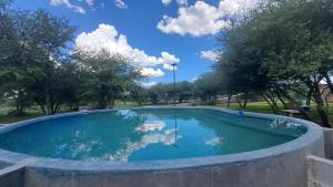 a swimming pool in a park with trees and clouds in the sky at The Spot at Ghanzi in Khemsbok