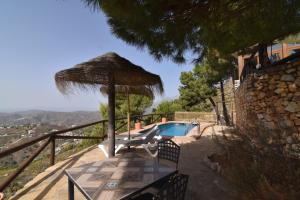 a table with a straw umbrella and a swimming pool at Finca La Sierra with private Pool in Cómpeta
