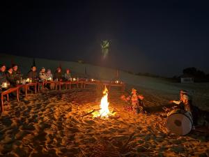 a group of people sitting around a fire on the beach at Desert Vista Camp Jaisalmer in Jaisalmer