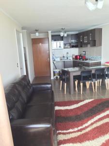 a living room with a leather couch and a kitchen at Arenamaris Apartment in Algarrobo