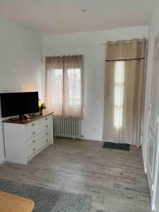 a living room with a tv and a dresser and two windows at Agreable studio proche du circuit du Mans in Arnage