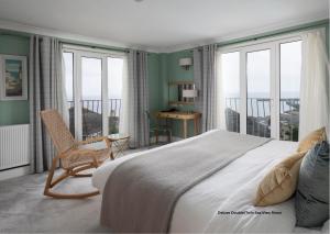 a bedroom with a large bed with a chair and windows at Hotel Penzance Harbour View in Penzance