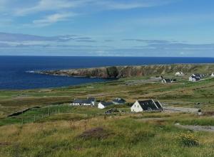 a group of houses in a field next to the ocean at Teach Hudi Beag, Bar & Accommodation Bunbeg in Bunbeg