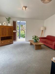 a living room with a red couch and a table at Kauri Coast Bungalow in Karekare